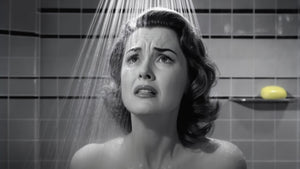 black and white image of sad woman seen from the shoulders up under the shower head with water coming down