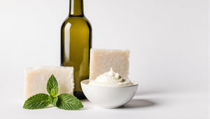 Bar of soap, bottle of olive oil, and bowl of coconut oil on a white background