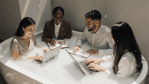 Four people in a bubble bath using laptops and notebooks